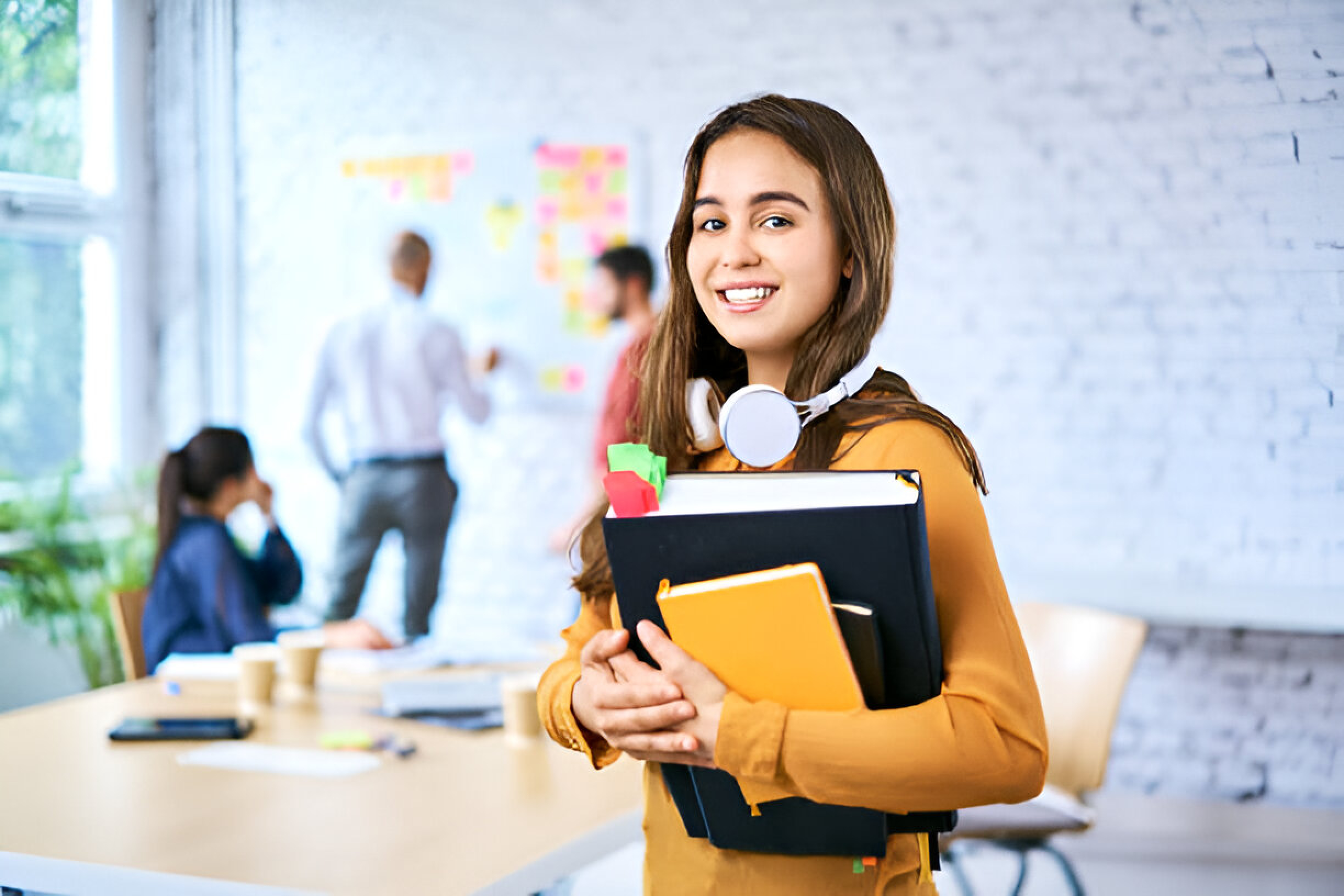A smiling woman holds a folder, standing confidently in front of a table, representing Veron's exam preparation success.