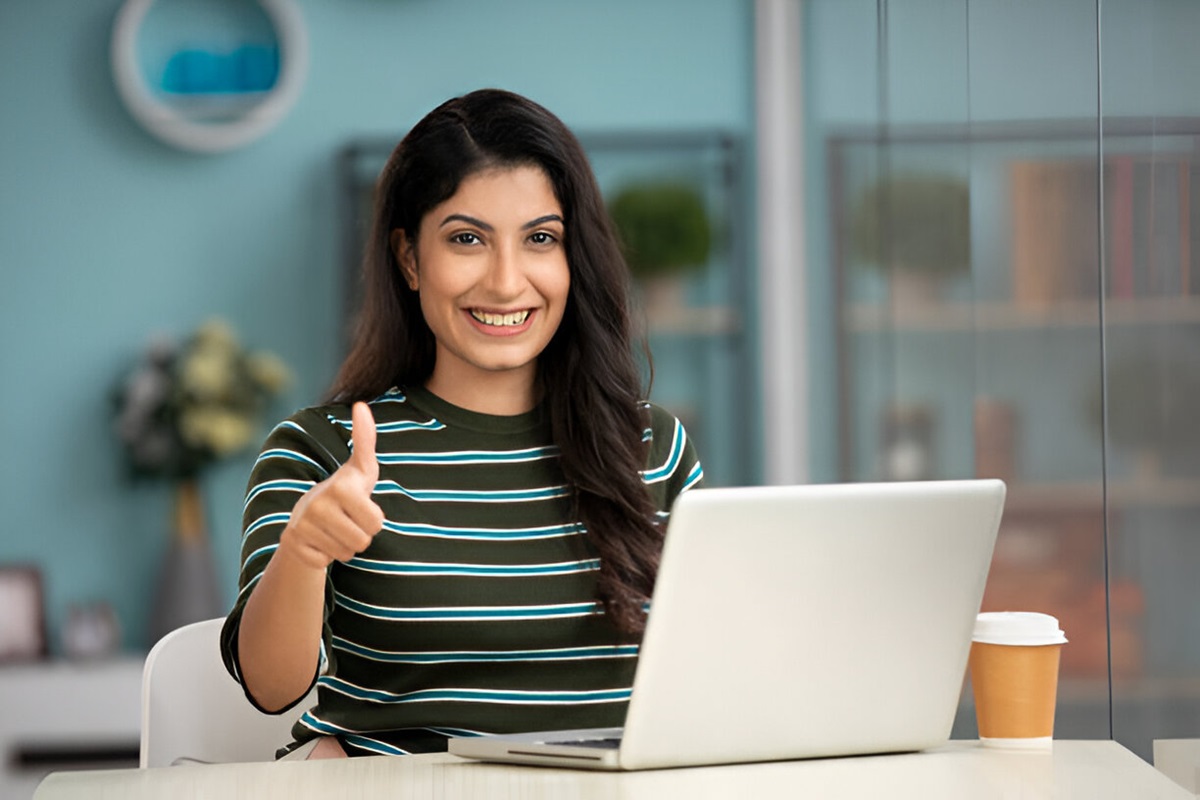 A woman at a desk with a laptop, smiling and giving a thumbs up, representing Veron, the Best Coaching in Amritsar