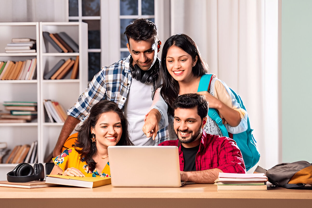 A group of young individuals gathered around a table, engaged with a laptop, celebrating their exam success in Amritsar.